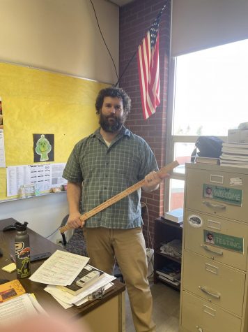 Teacher Jeremy Comstock holds the Needle of Fate, the meter stick which he spins atop a stool to select students for various activities. 