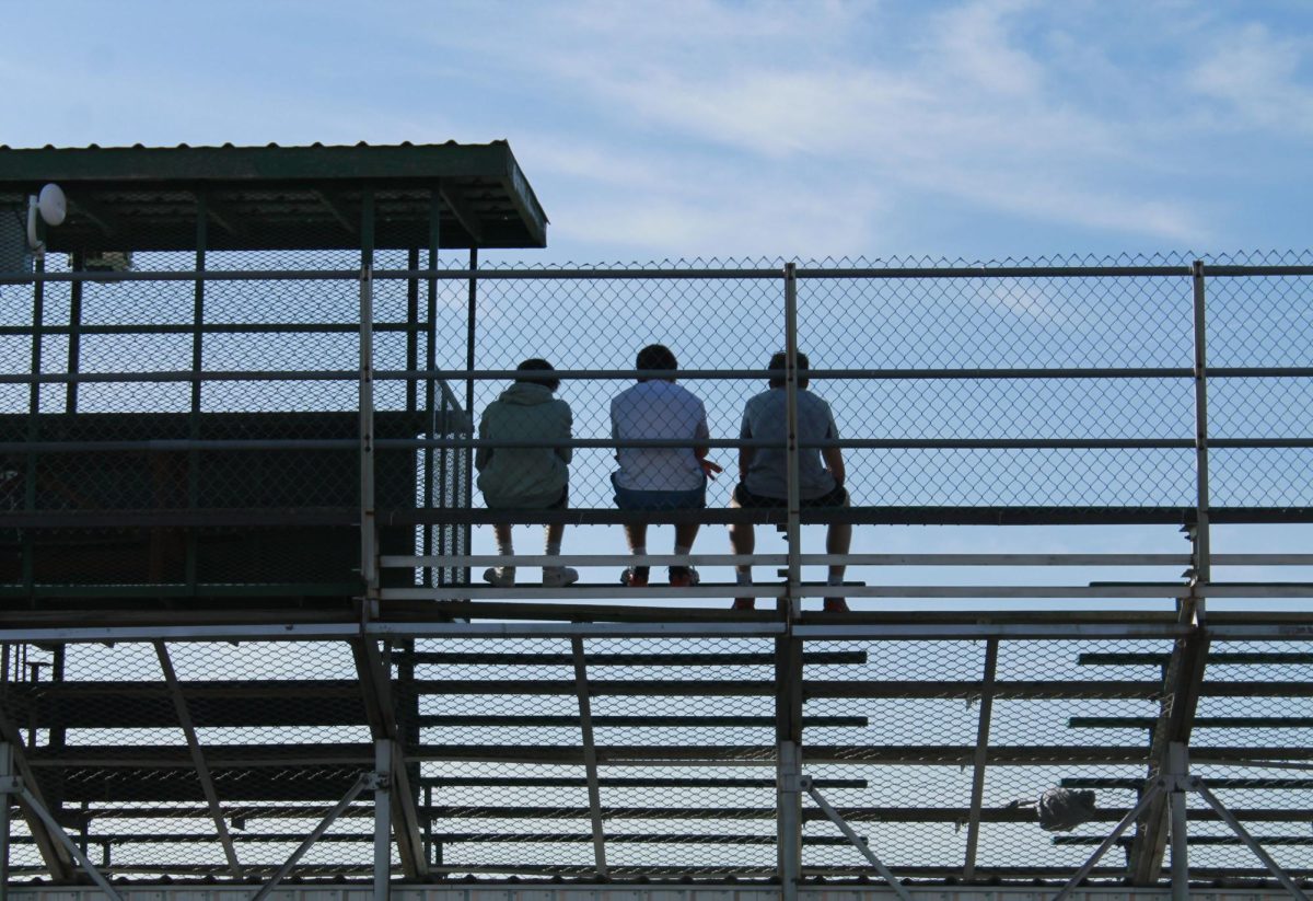 Three boys sit looking out on the track while their classmates run the mile for gym class.