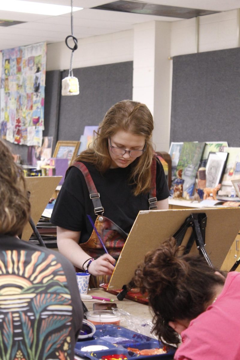 A girl carefully paints her piece and is focused on her painting.
